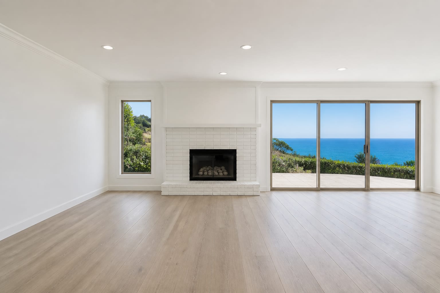 Empty living room with a white brick fireplace and a slider to the ocean