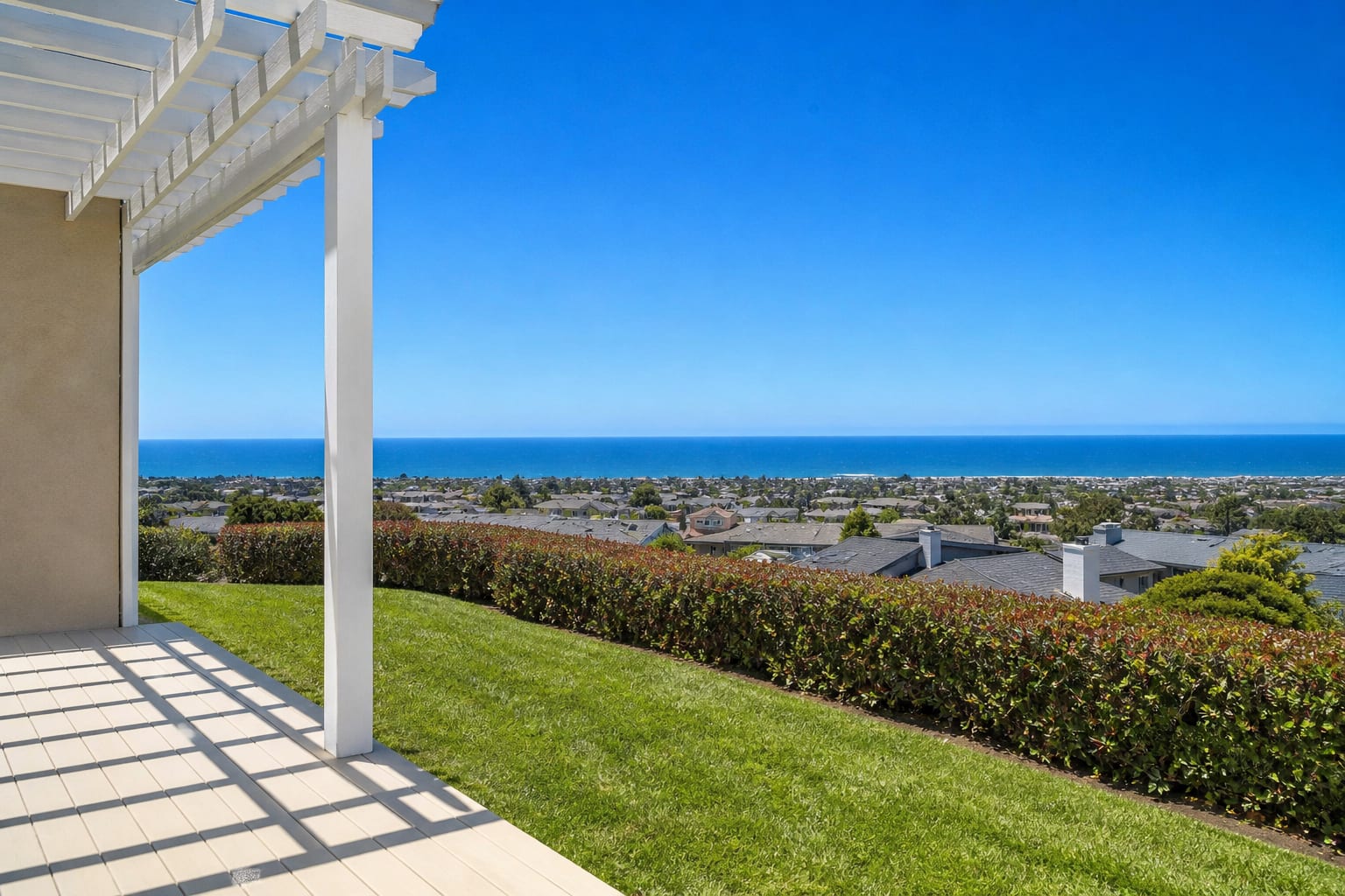 Patio and white pergola overlooking a coastal neighborhood and the ocean
